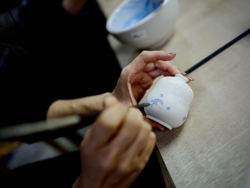 Somebody paints blue decorations on a white clay pot.